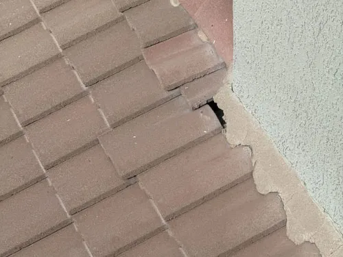 Cracked and displaced tile at a roof-wall junction showing storm damage on a Tucson home