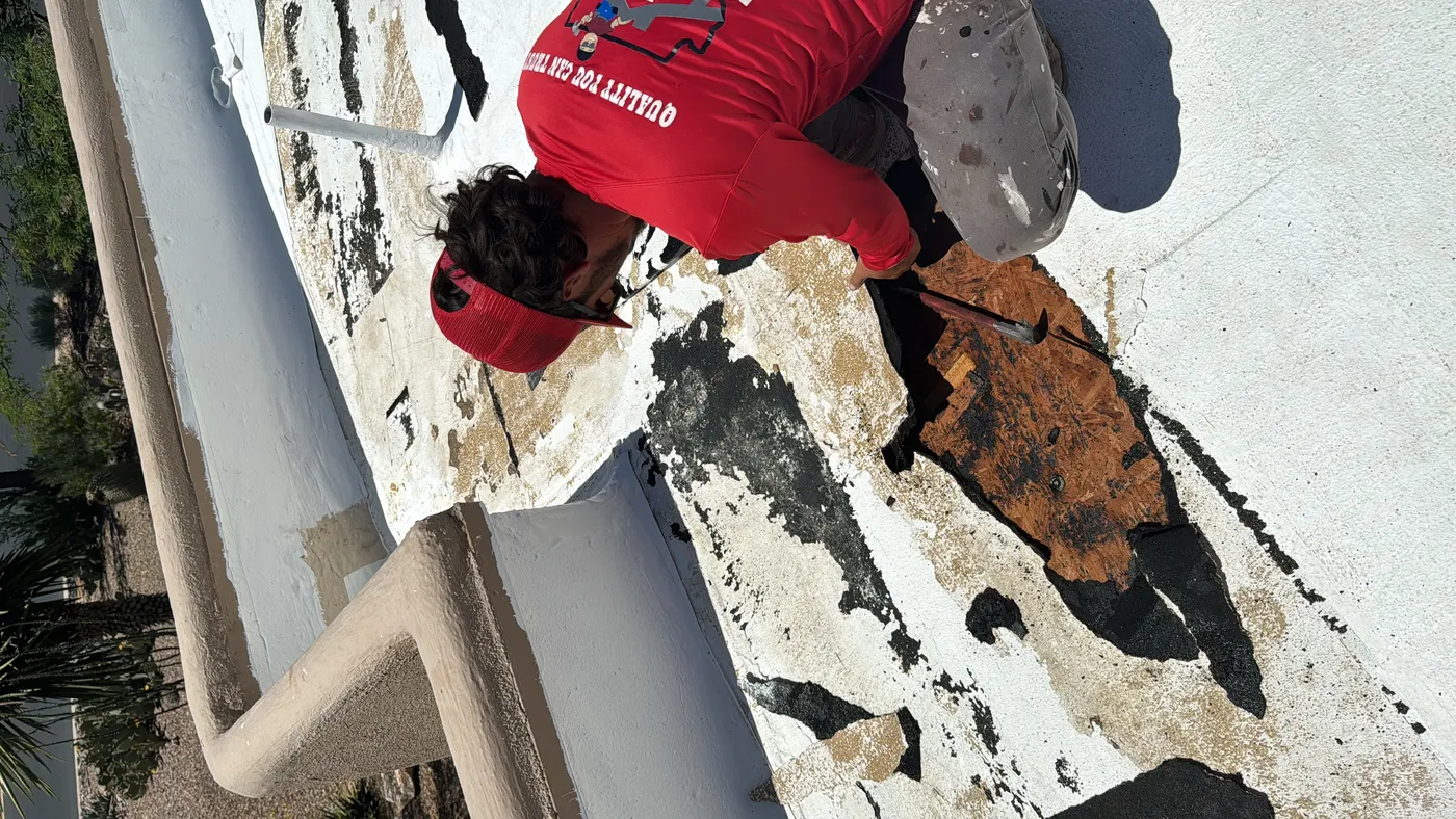 DC Roofing worker removing damaged flat roof membrane revealing the wood deck below