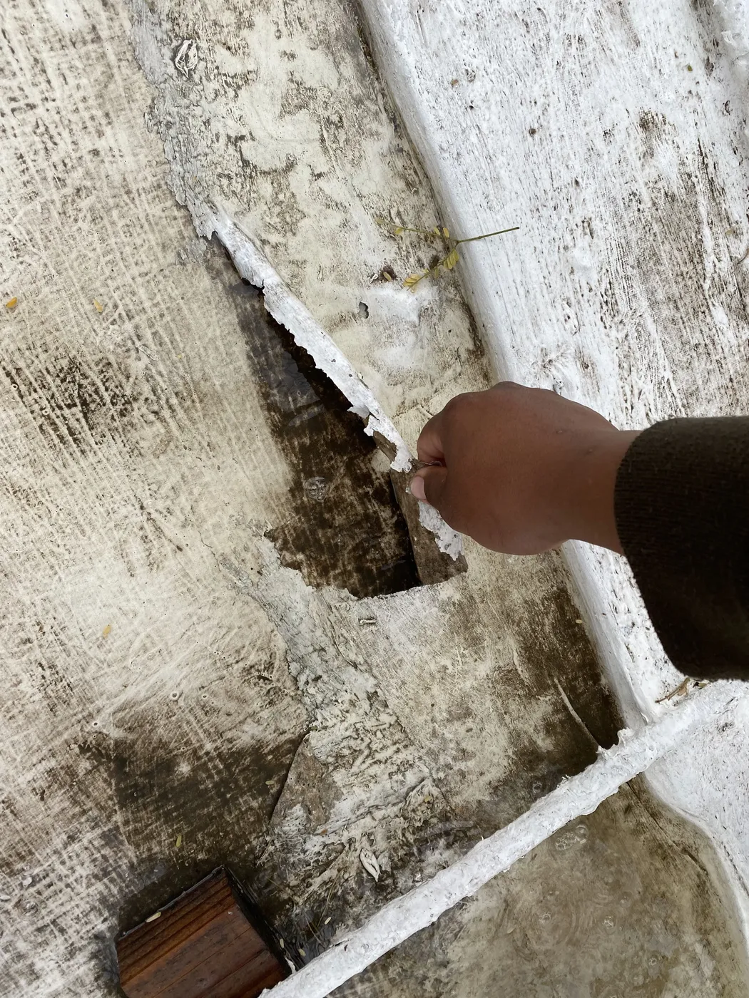 Hand pointing to large hole in deteriorated roof deck requiring emergency repair in Tucson